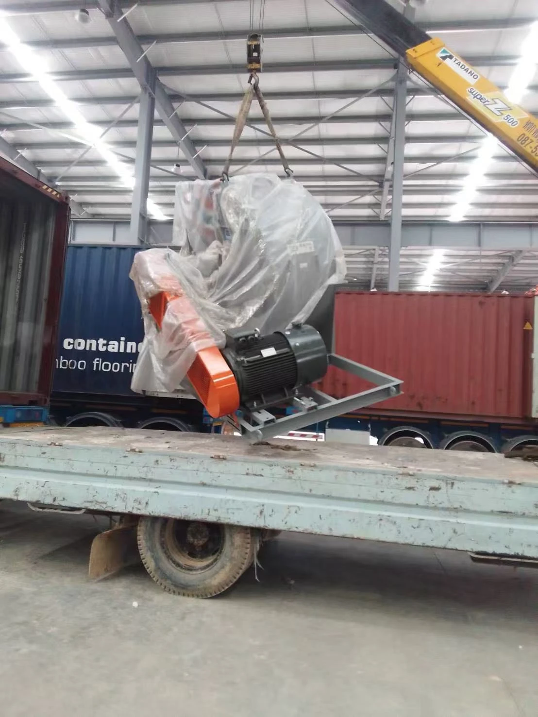 Wrapped industrial equipment being lifted above a truck during unloading