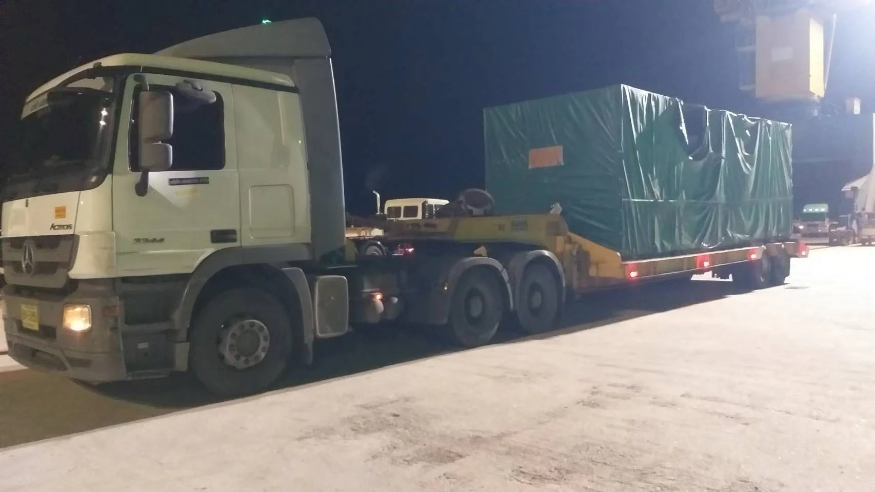 Large covered cargo on a low trailer at a night-time handling site