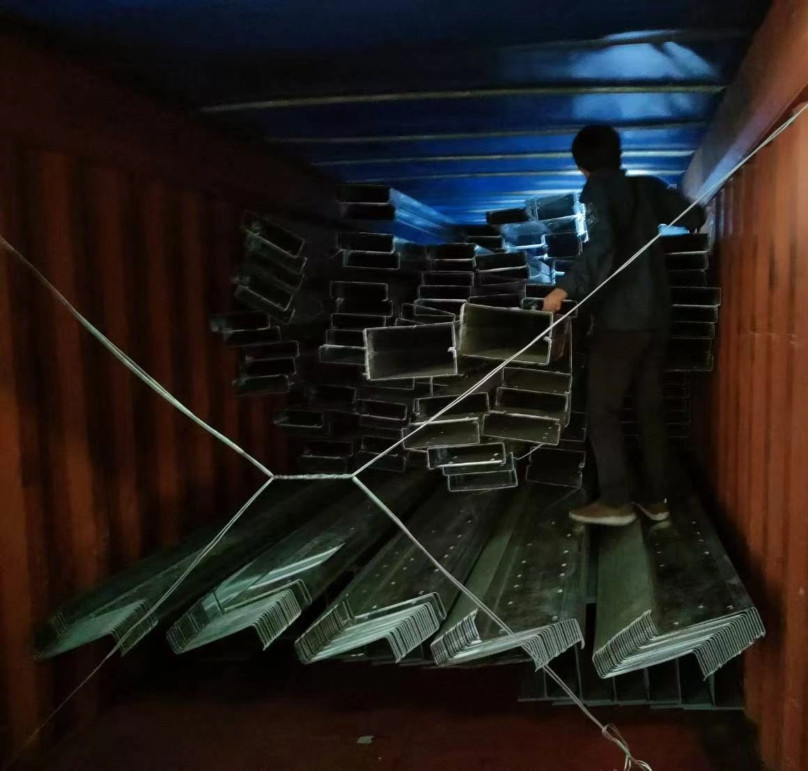 A person standing beside stacked steel sections inside a shipping container
