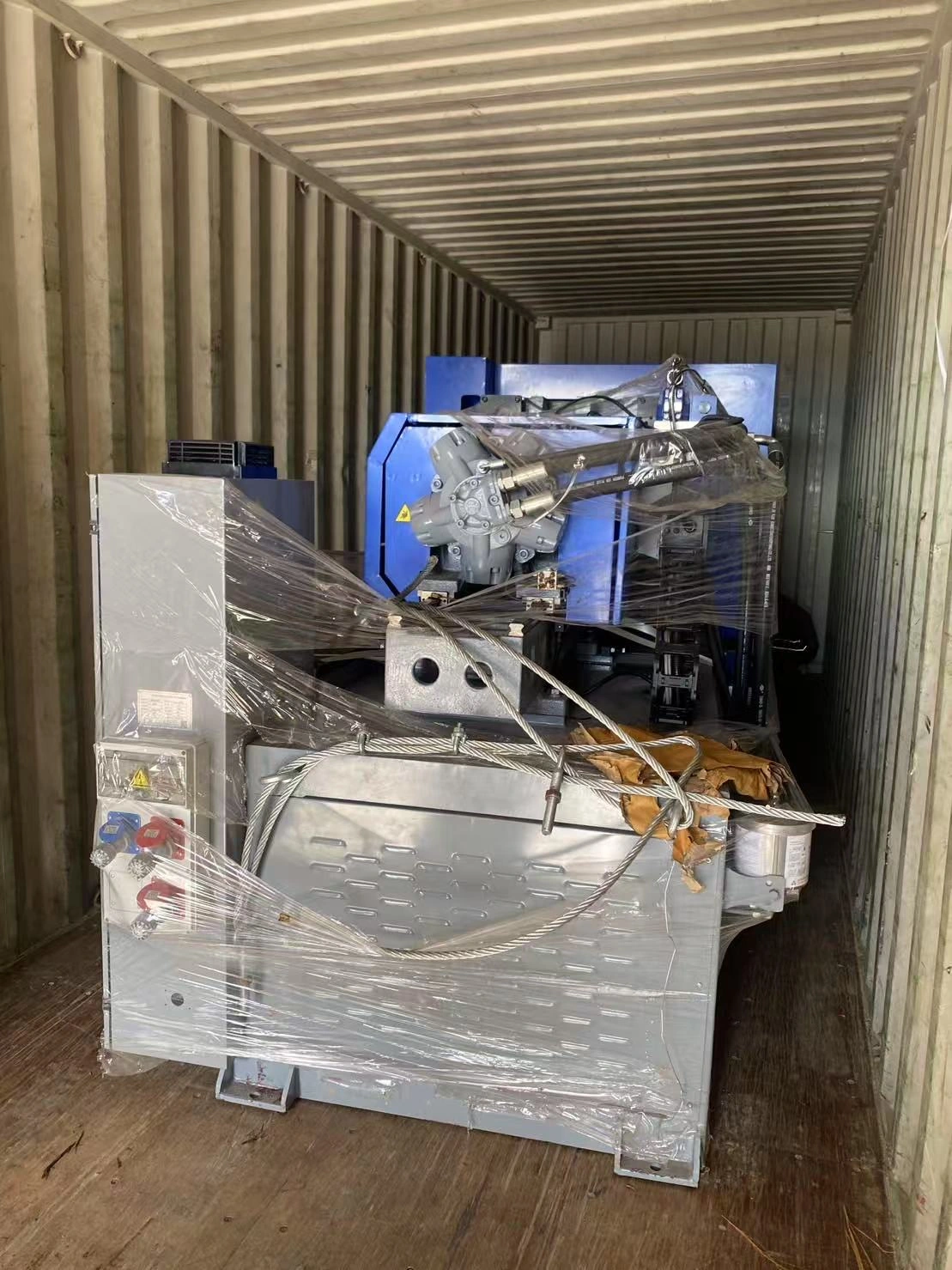 Wrapped equipment viewed inside a shipping container, showing the equipment body and surrounding container interior.